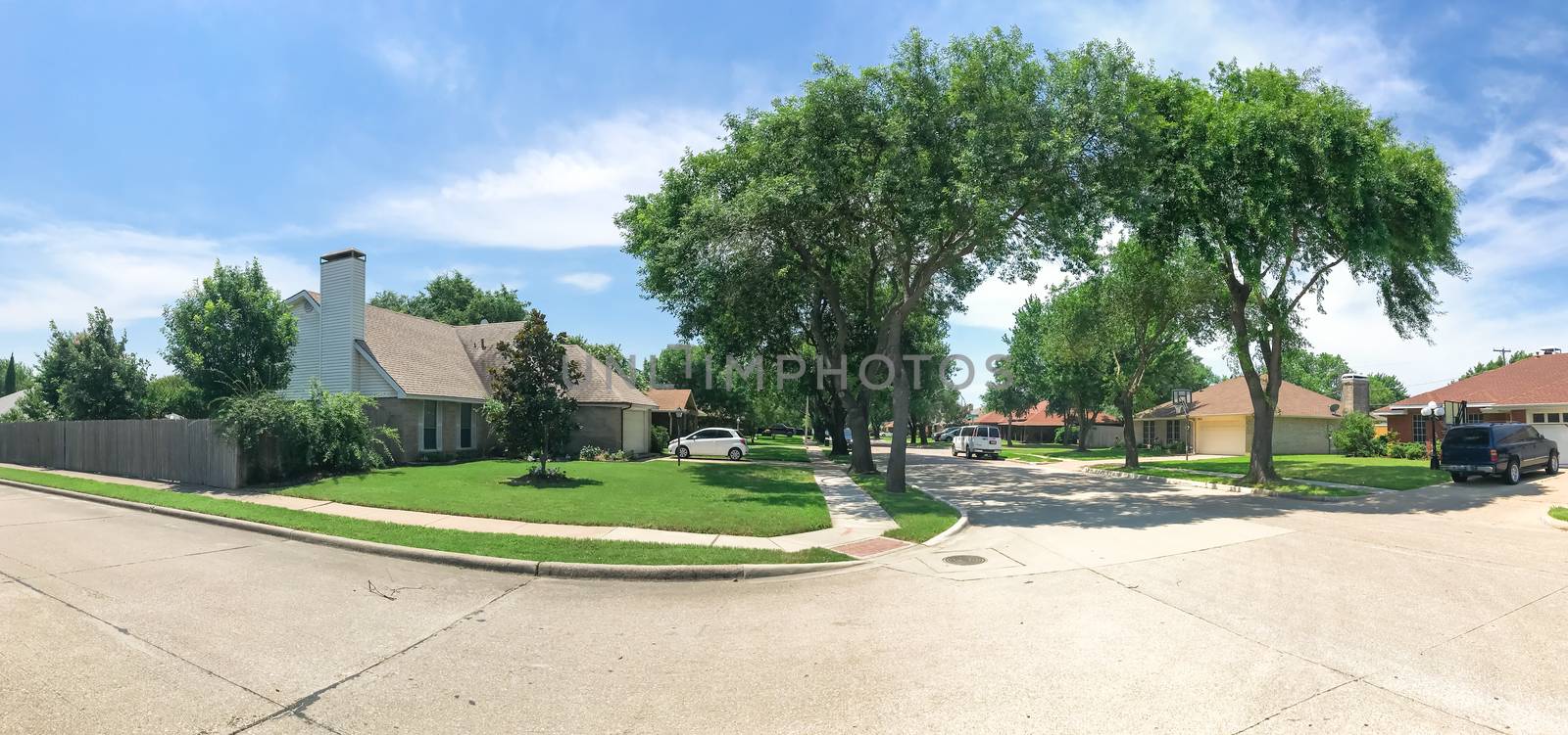 Panorama tall oak trees canopy street and bungalow style single-family detached house neighborhood in West of Dallas, Texas, USA. Summertime with cloud blue sky, cars on street, near sidewalk pathway
