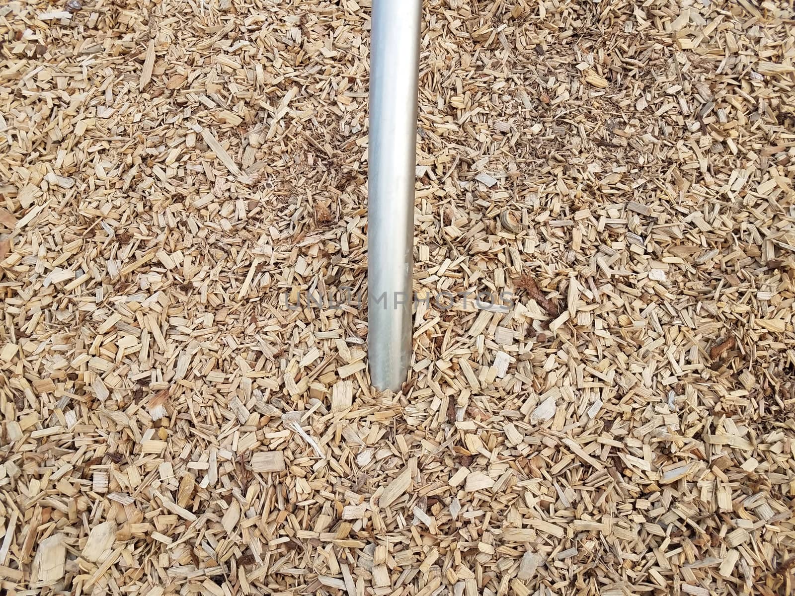 silver metallic bar or rod in brown mulch or wood chips