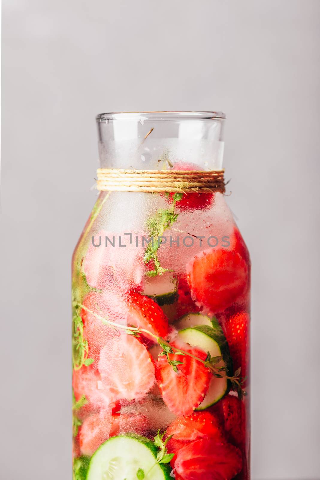 Part of Bottle with Infused Water, Fresh Strawberry, Sliced Cucumber and Springs of Thyme. Vertical Orientation.