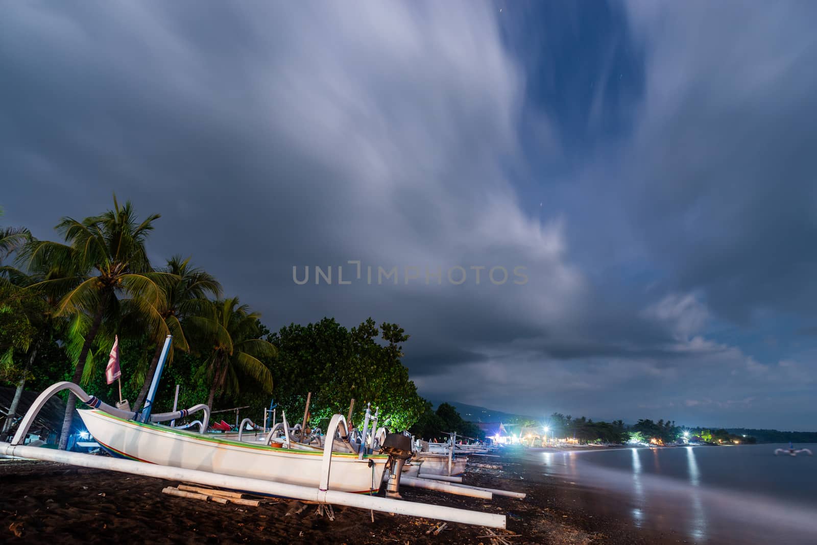 Traditional fishing boats on Amed beach at night in Bali, Indonesia. Long exposure photography resulting in motion blur in the clouds, the sea and the trees.