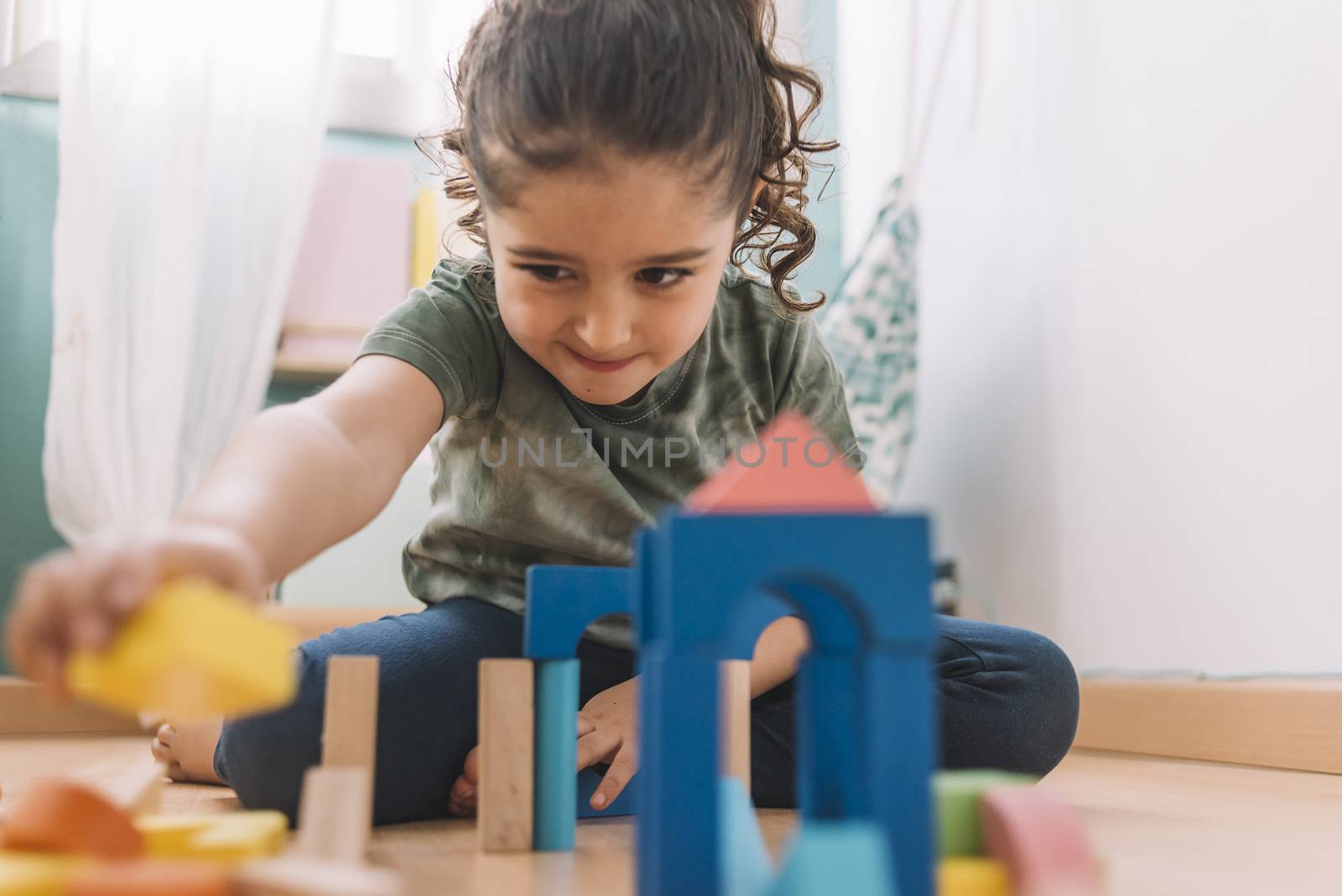 child little girl playing constructions on the floor with wooden building block toys in her room or kindergarten, educational toys for creative children