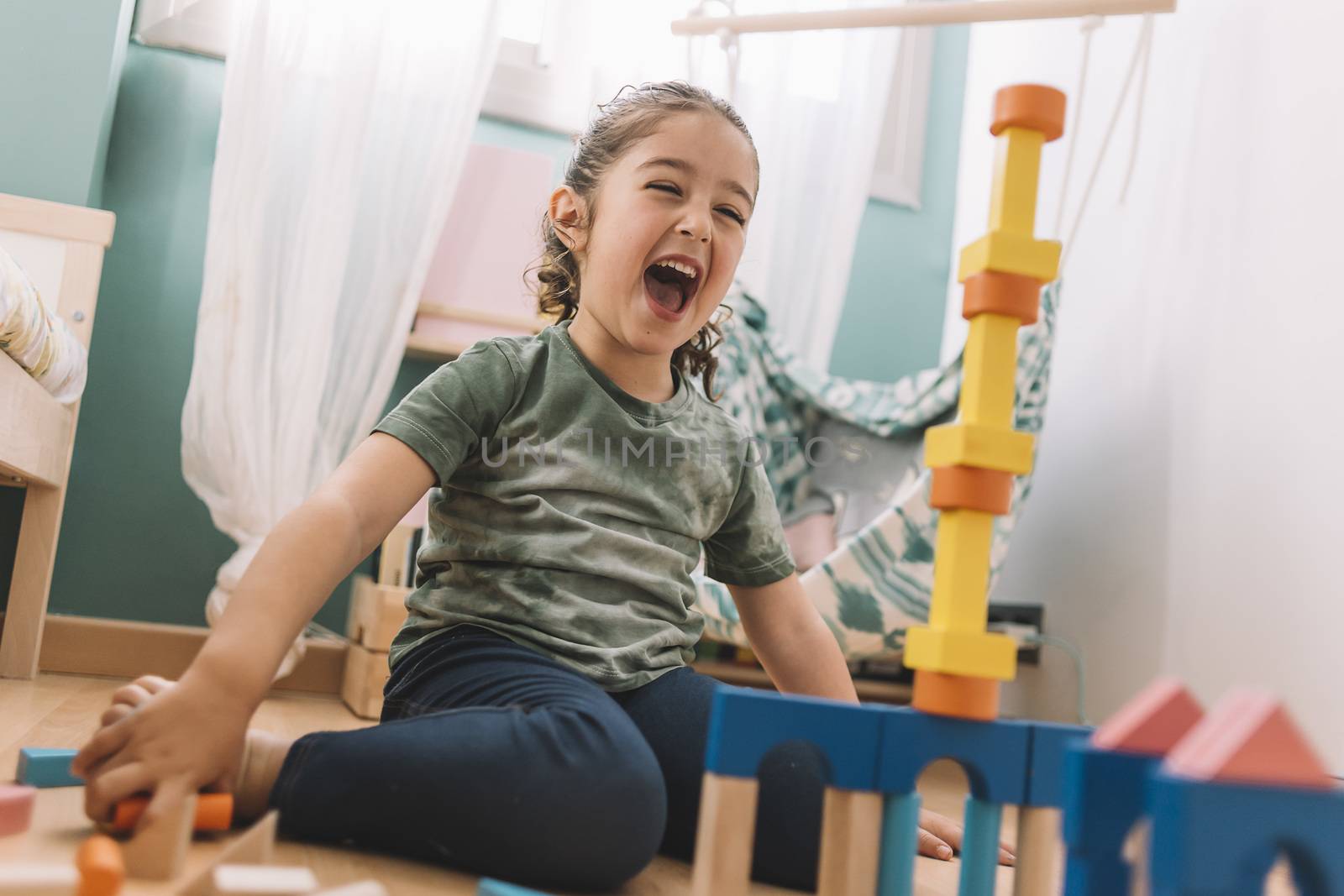 funny little girl laughing while playing happy in the floor with colorful wooden building block toys at home or kindergarten, educational toys for creative children