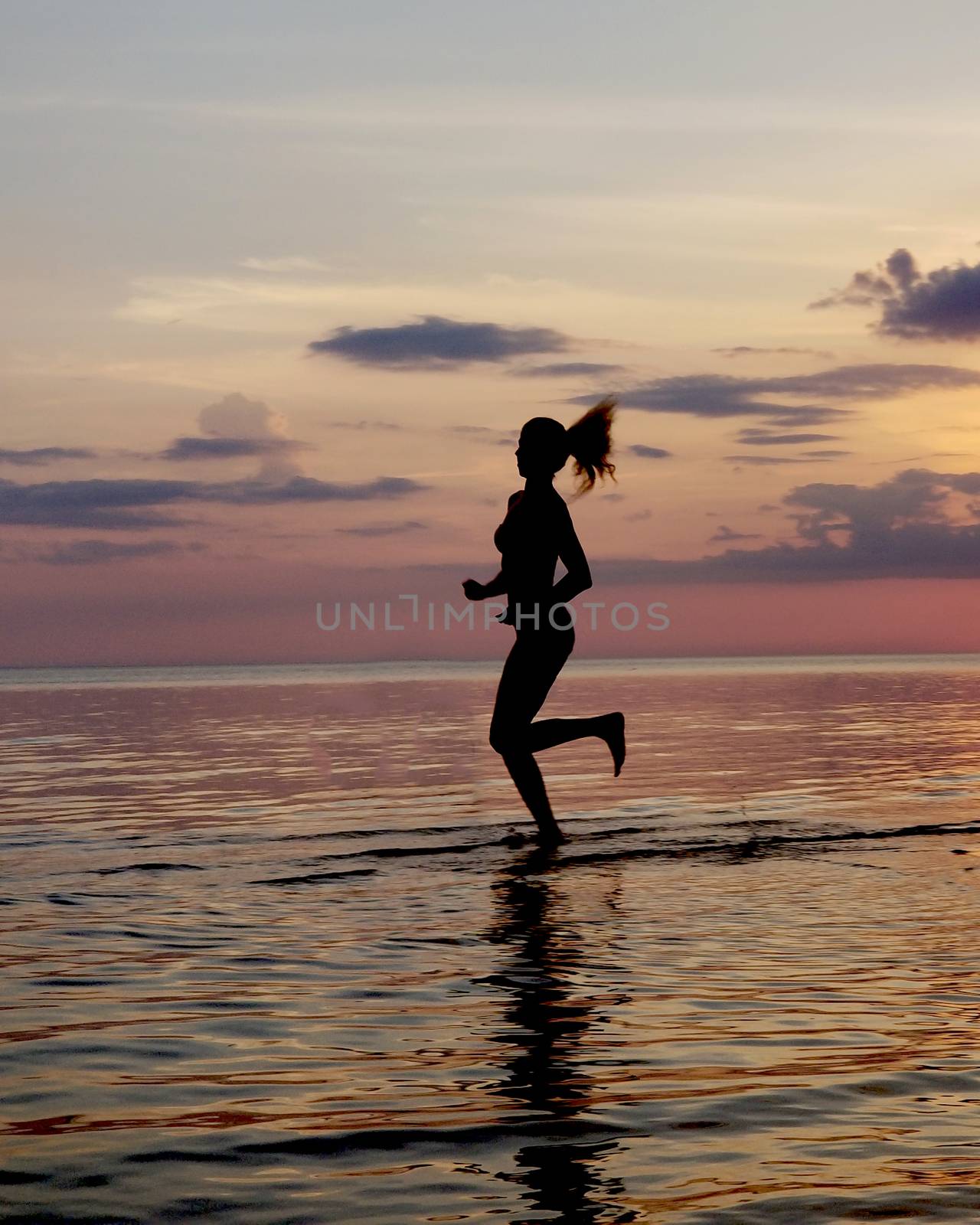 silhouette of a girl run on the beach sand. Shooting against the sun. Sunset over the sea.