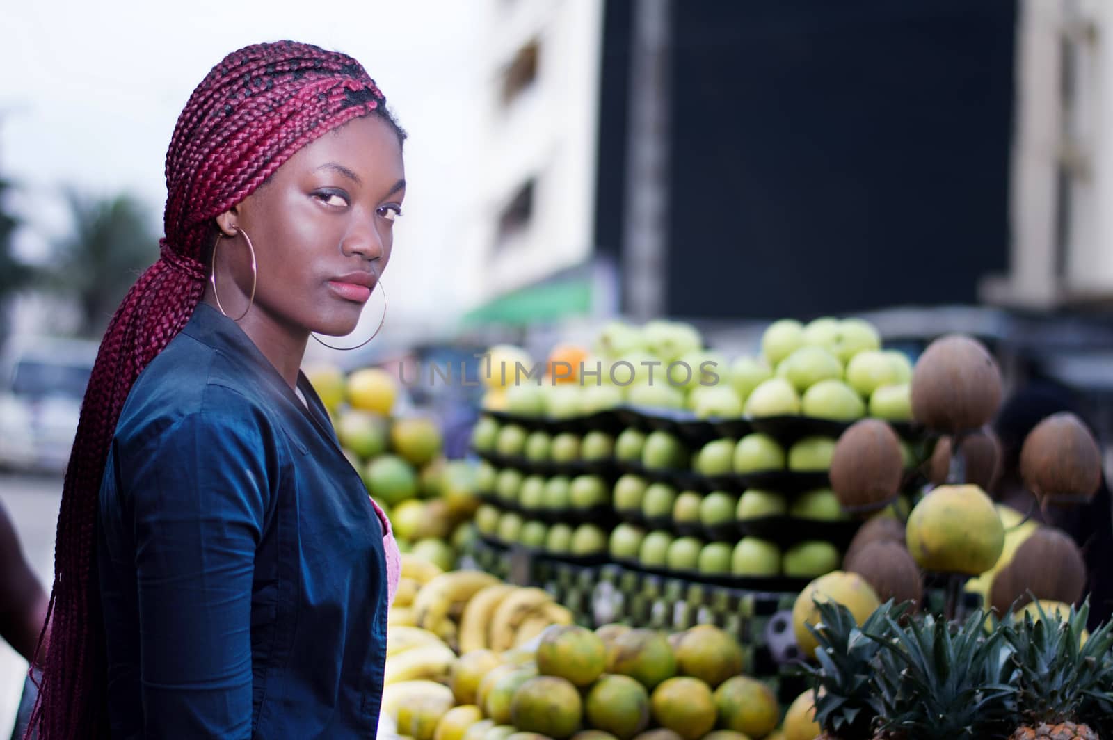 young woman standing in front of shelves of fruit, looking at the camera.