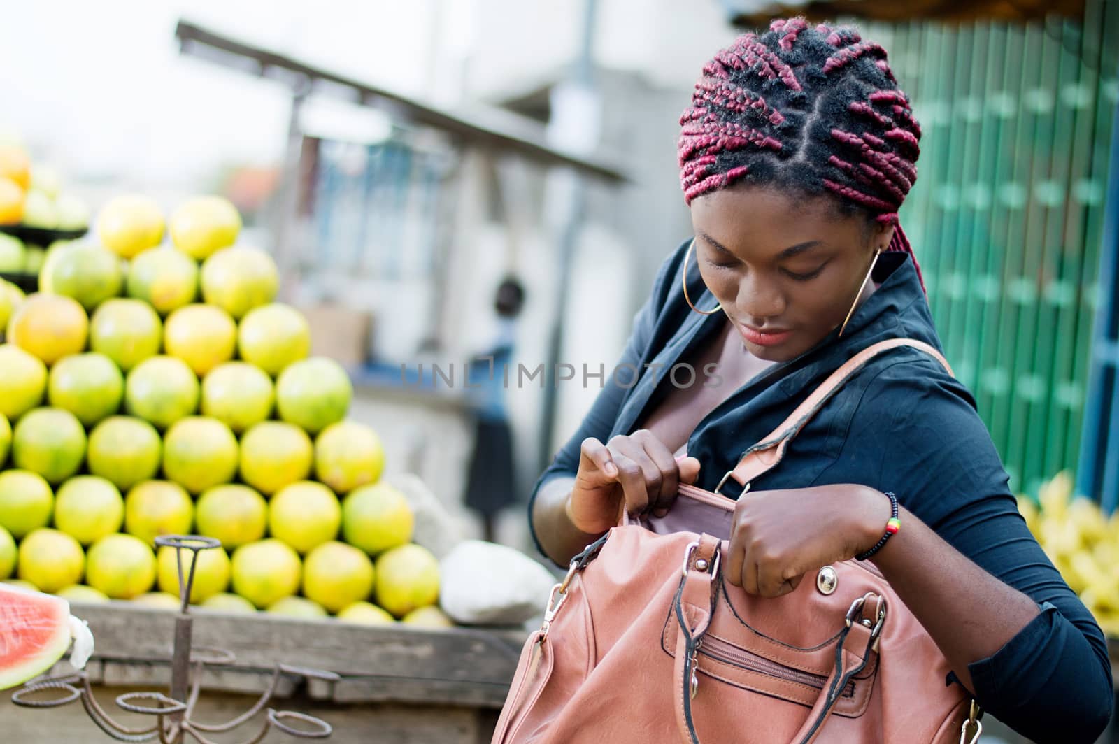 young woman standing in front of a fruit shelf, rummages in her handbag.