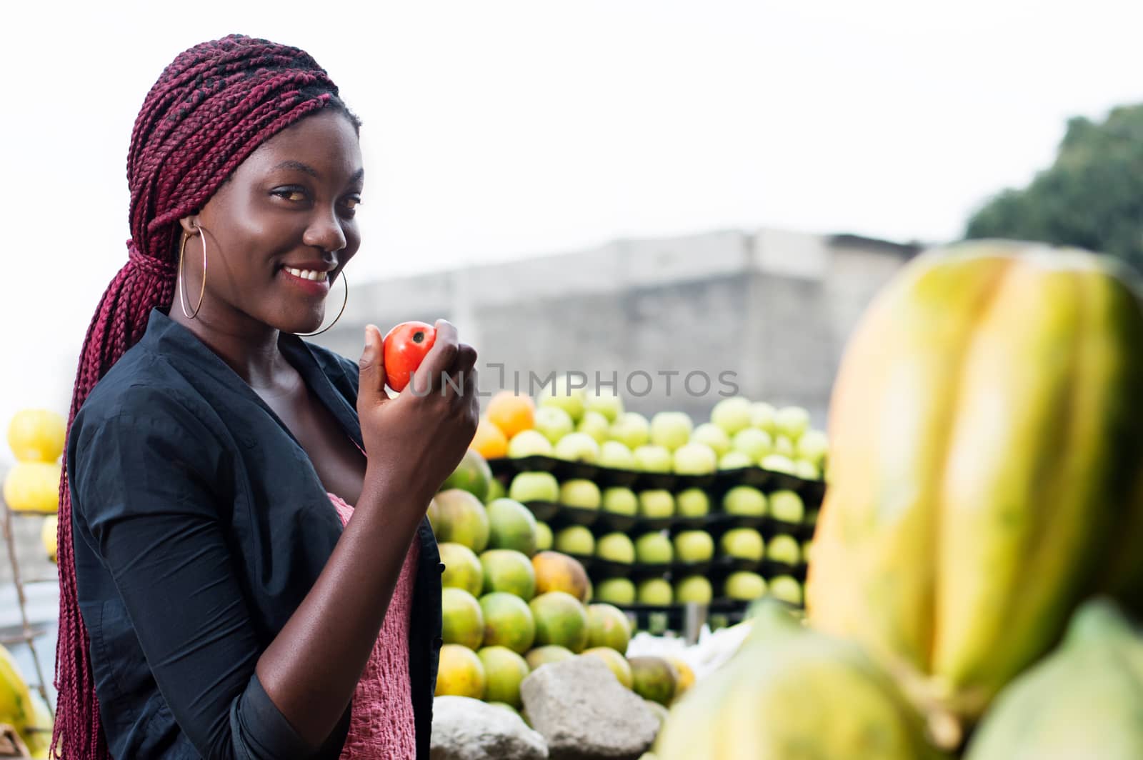 smiling young woman shows a ripe tomato looking at the camera.