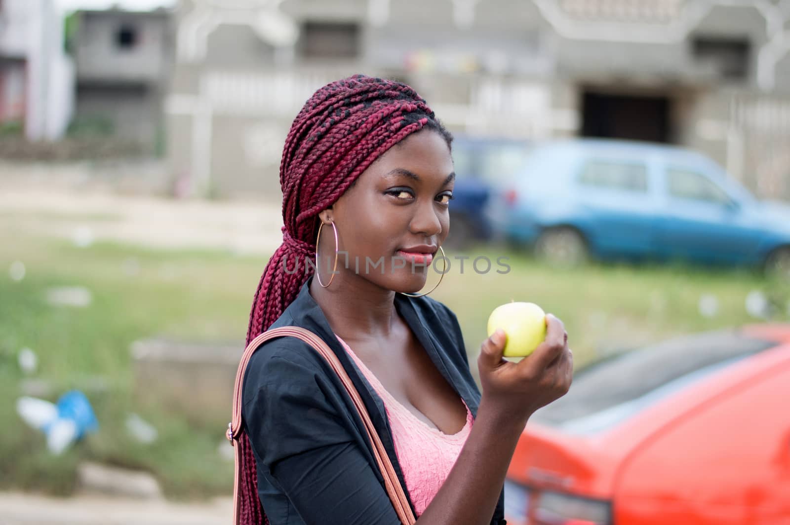 young and beautiful woman holding an apple is standing at the edge of the road.