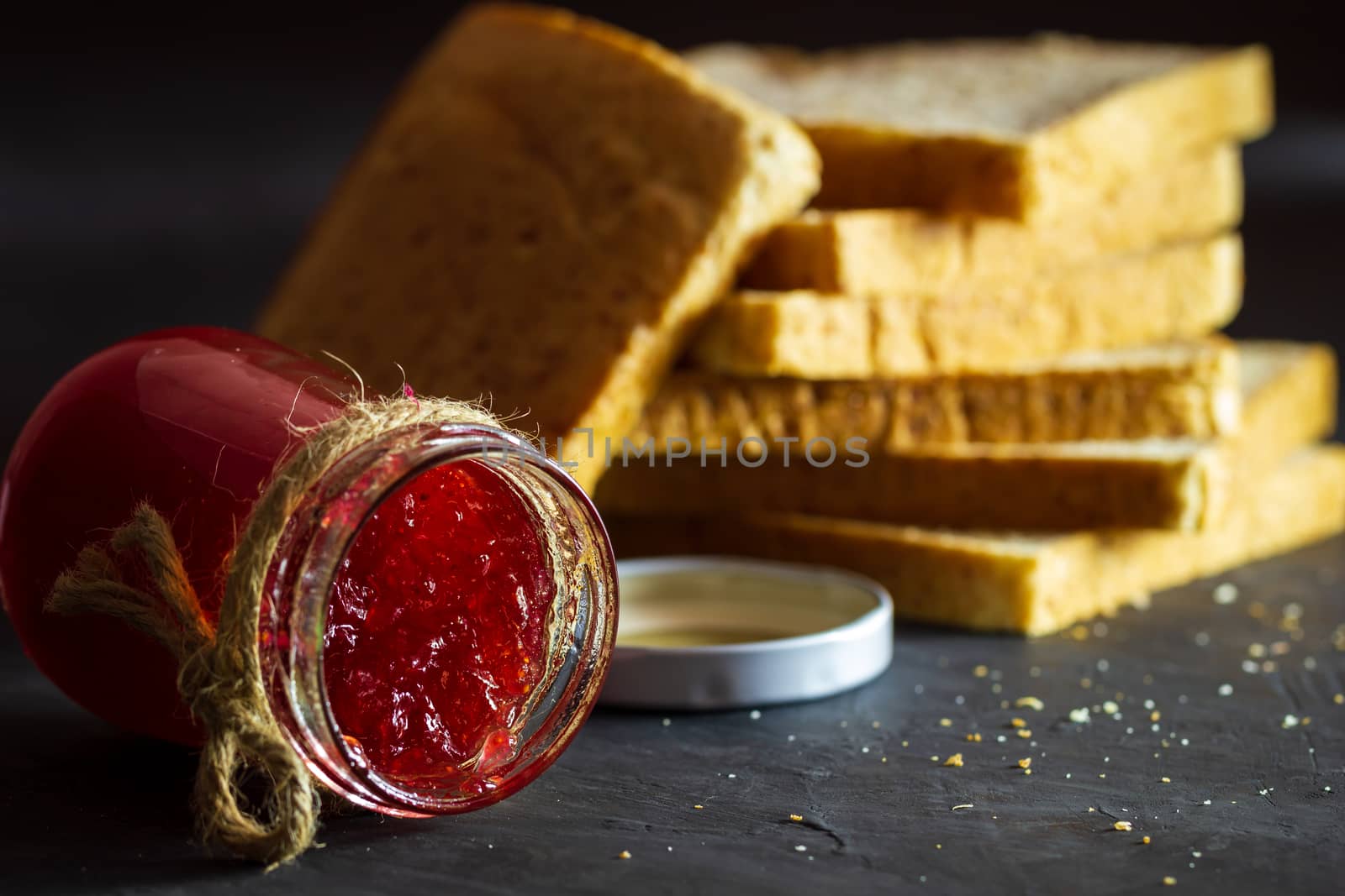 Strawberry jam bottle and whole wheat bread are stacked on a black background. Concept of breakfast and healthy food.