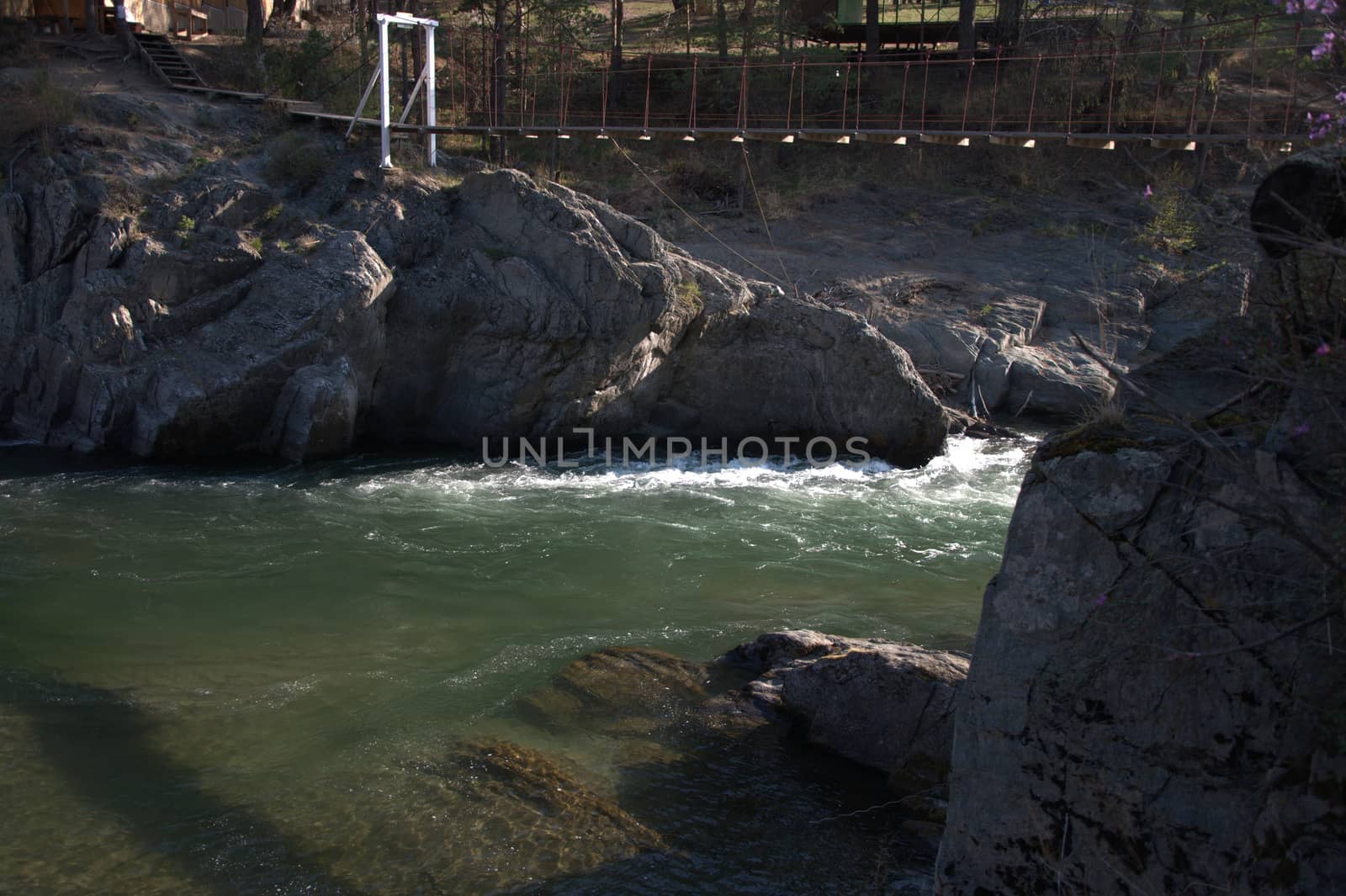 Suspended pedestrian bridge over a stormy mountain river. Altai, Siberia, Russia.