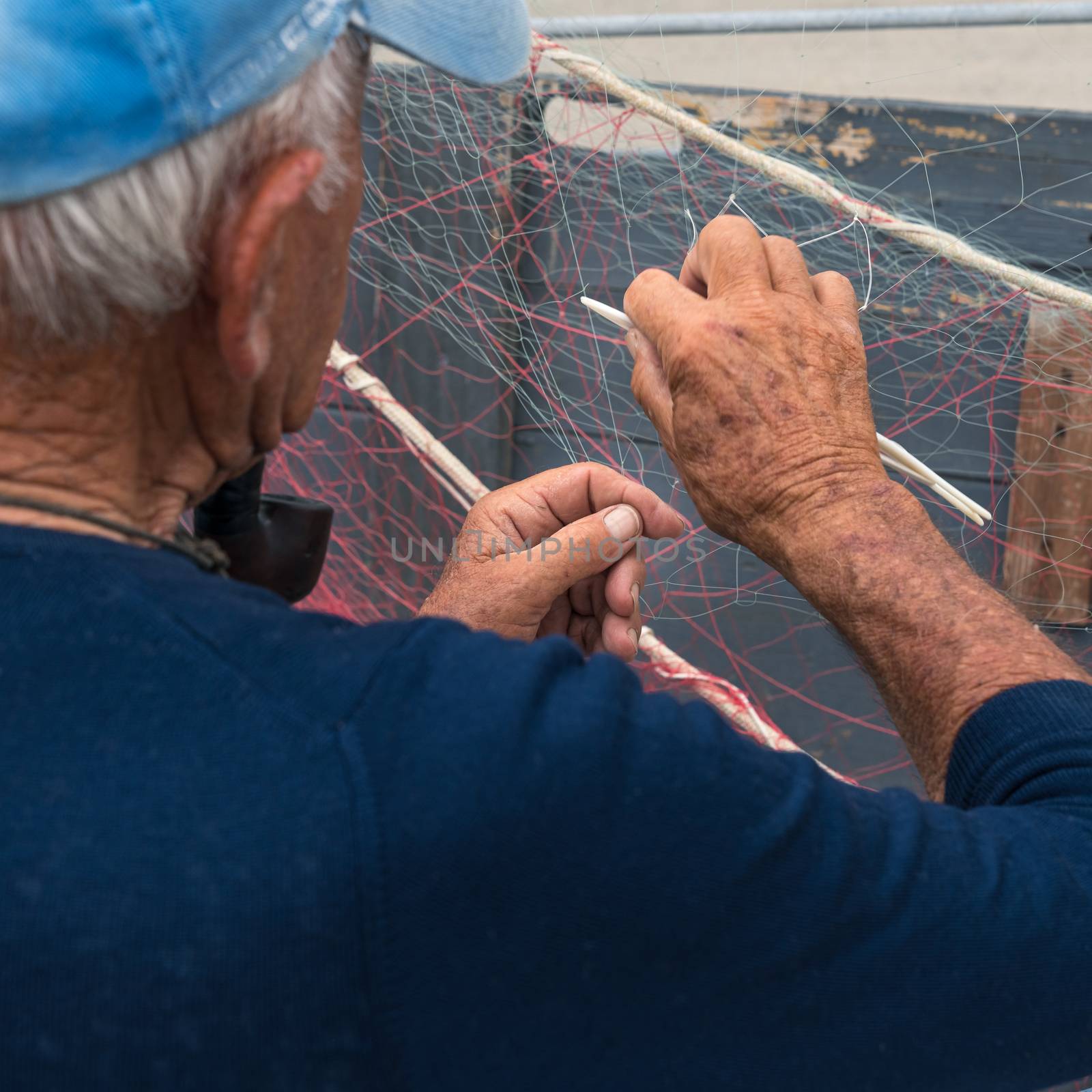 Old fisherman reparing fishing net, sitting with pipe in his mouth.