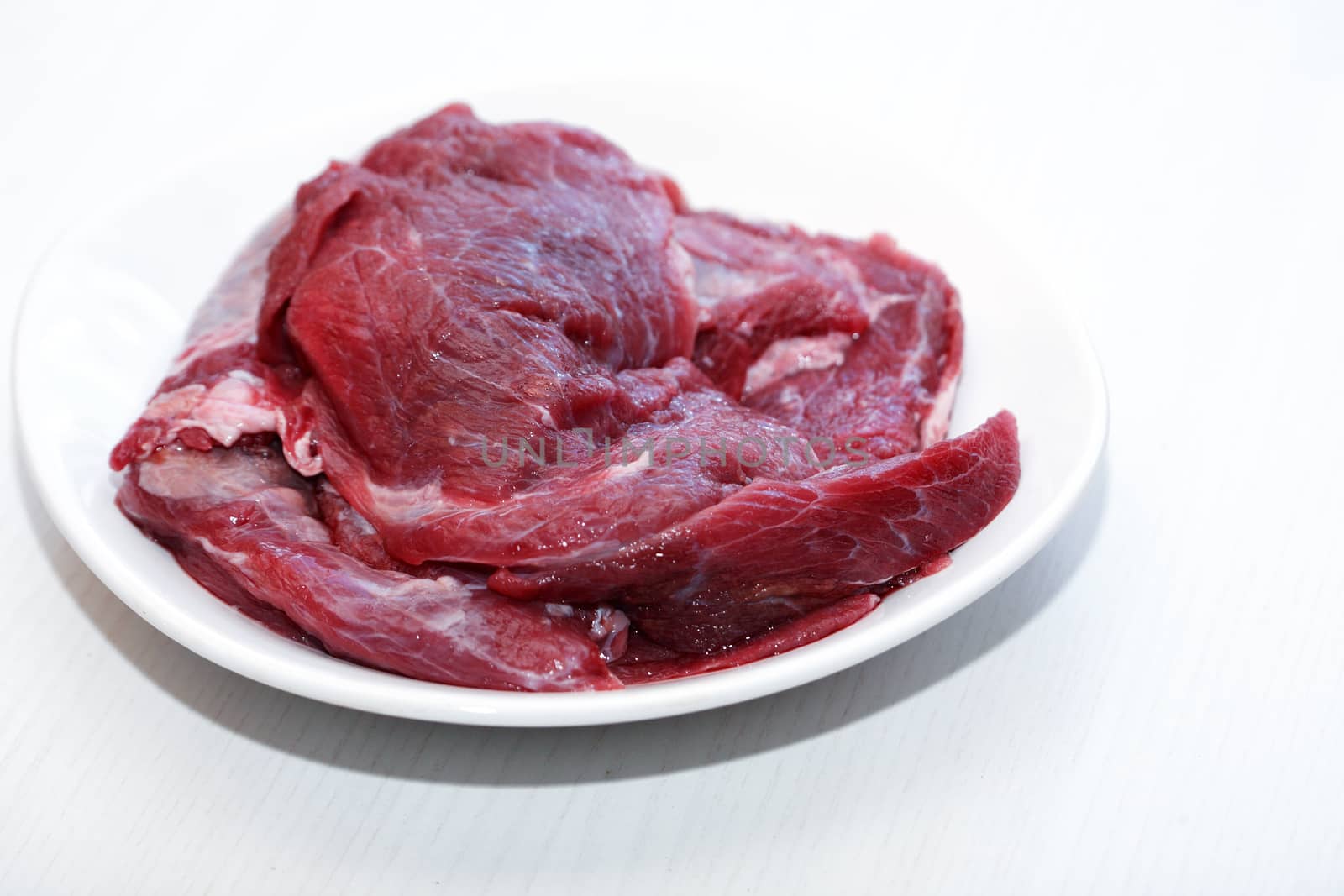 Portion of raw beef meat for cooking on white plate