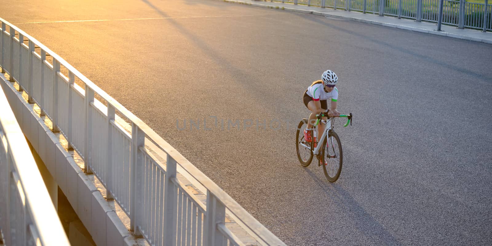 Young Woman Riding Road Bicycle on the Bridge in the City at Sunset. Healthy Lifestyle and Sport Concept. by maxpro