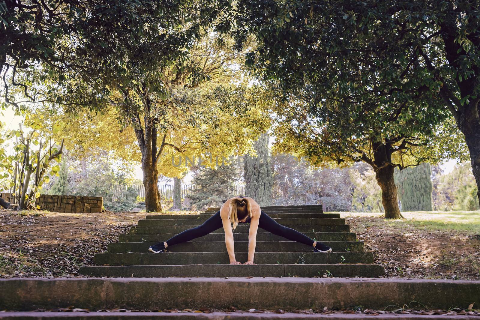 young woman runner doing some warm up exercises and stretching legs after running, sports girl at the park in morning with sunlight