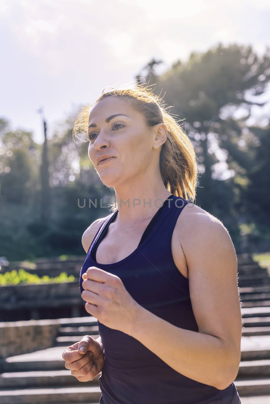 vertical portrait of young sports woman jogging during outdoor workout at the park at the morning with sunlight, sport and healthy lifestyle concept