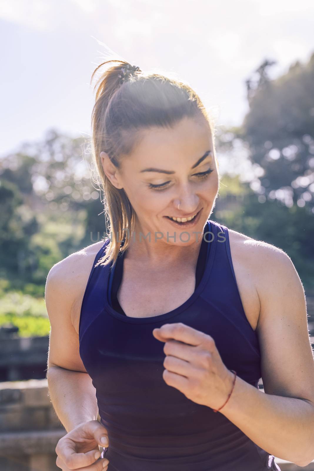 vertical portrait of happy sports woman running during outdoor workout at the park at the morning with sunlight, sport and healthy lifestyle concept