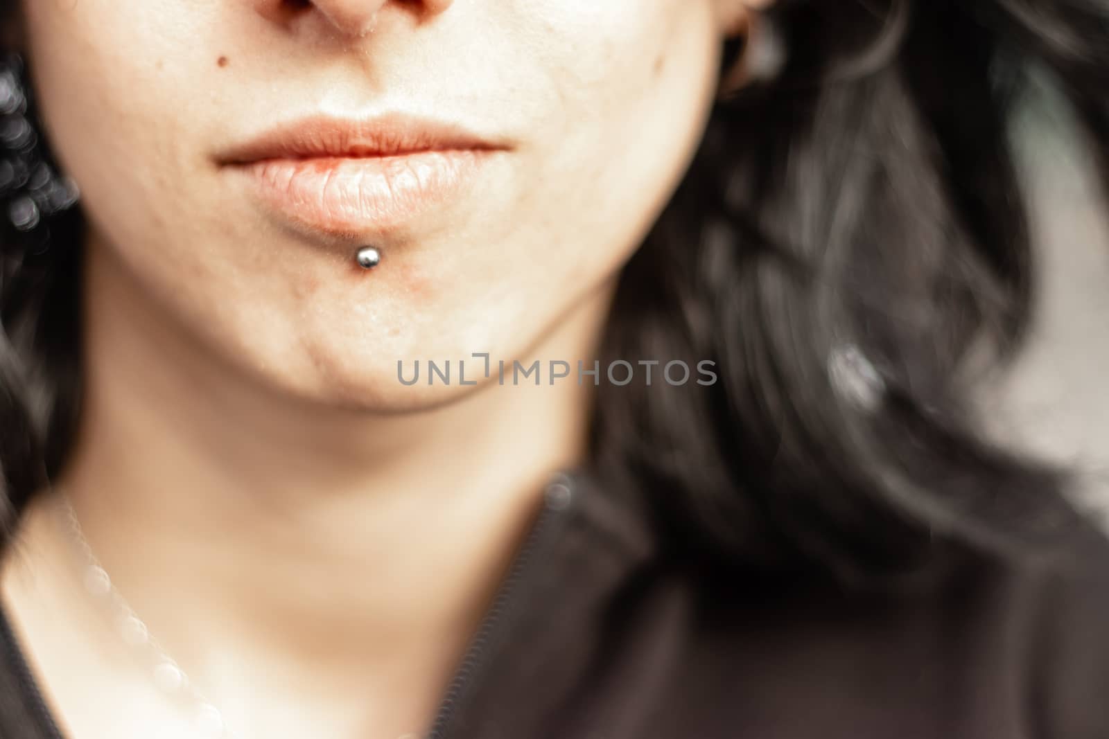 face expression from a black haired girl with metal chin piercing. black sweater on her.