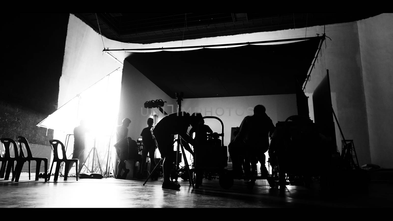 Behind the shooting of video online commercial production and film crew team working and setting light or camera or soft box and equipment set up in big studio in silhouette style