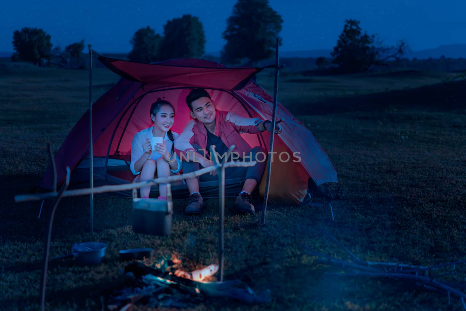 Couple of travelers spending time in tent near campfire