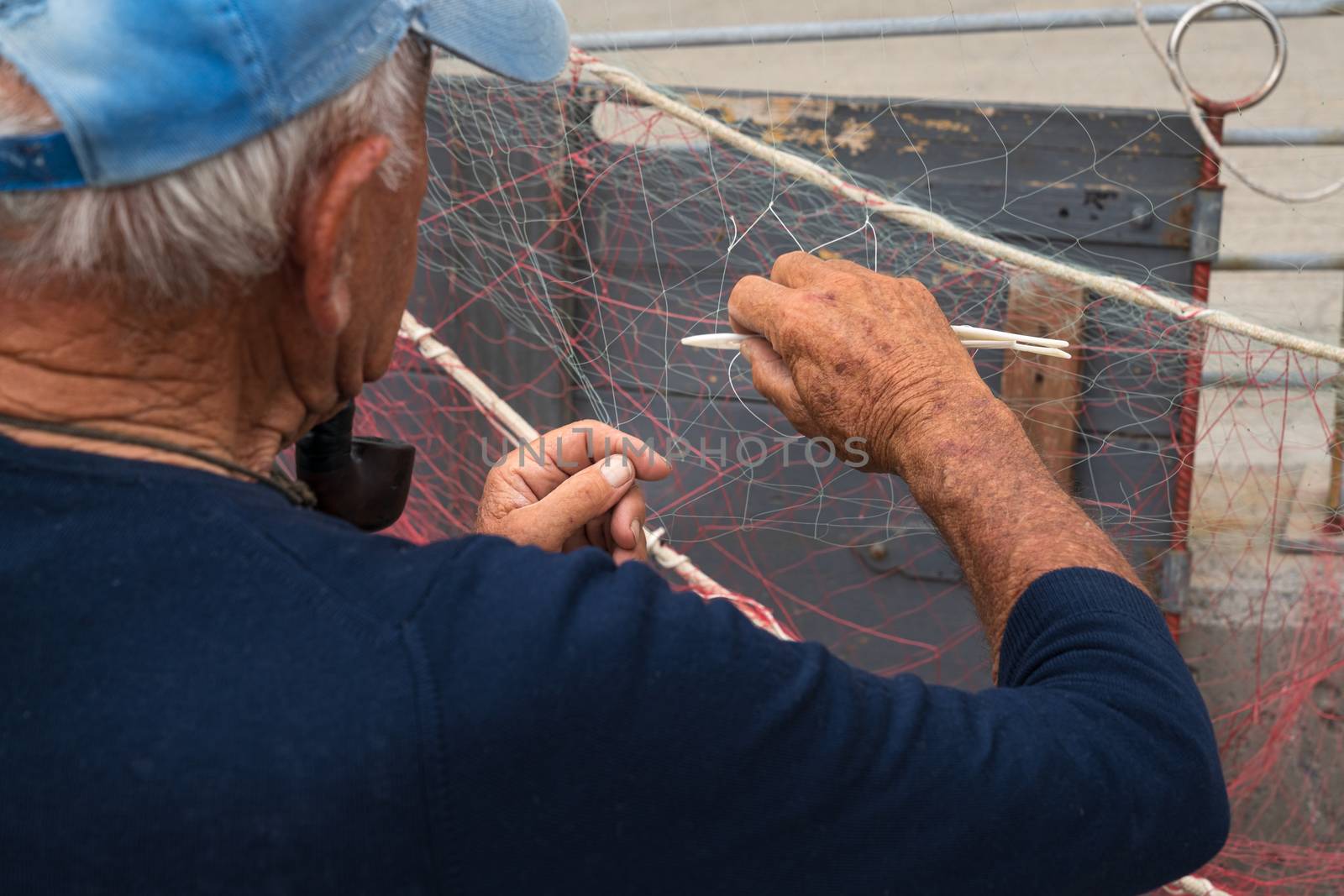 Senior fisherman is fixing a fishing net by Robertobinetti70