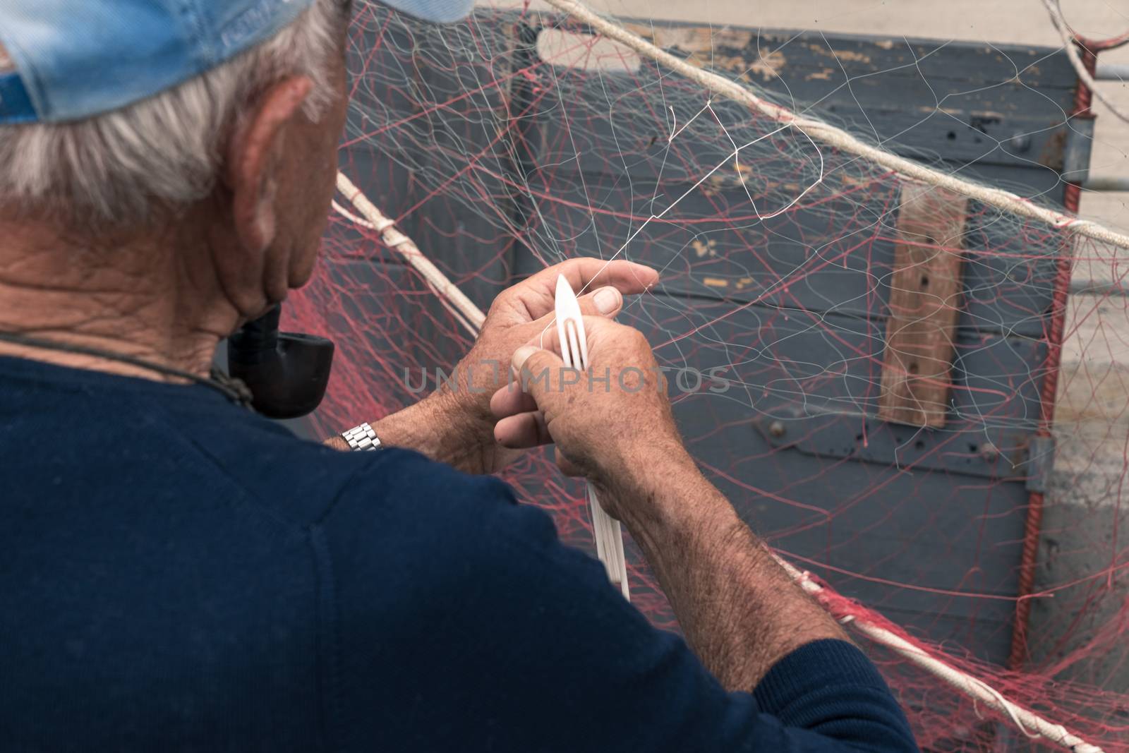 Old fisherman reparing fishing net, sitting with pipe in his mouth.