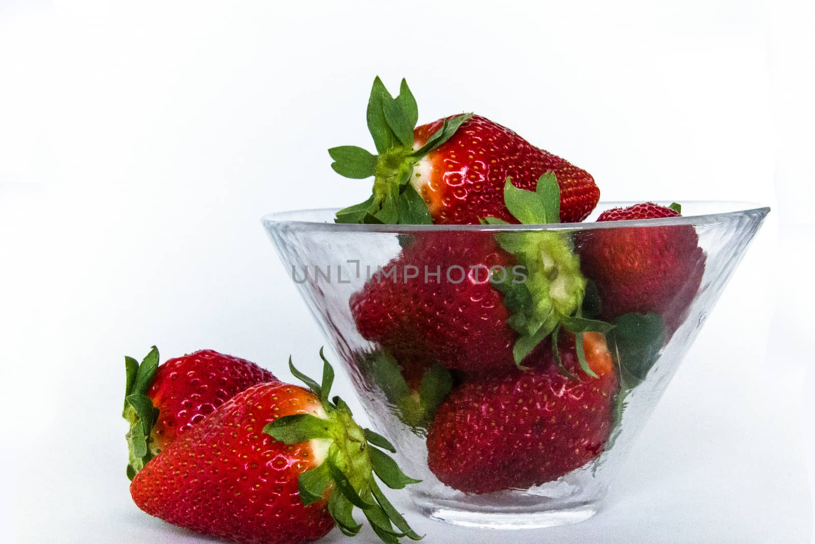 some strawberries in a glass cup and two of them outside