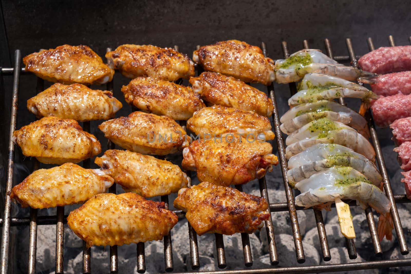 Mixed assortment of marinated meat, chicken, and prawns grilling on hot coals on a BBQ, summer outdoor party, delicious meal preparation