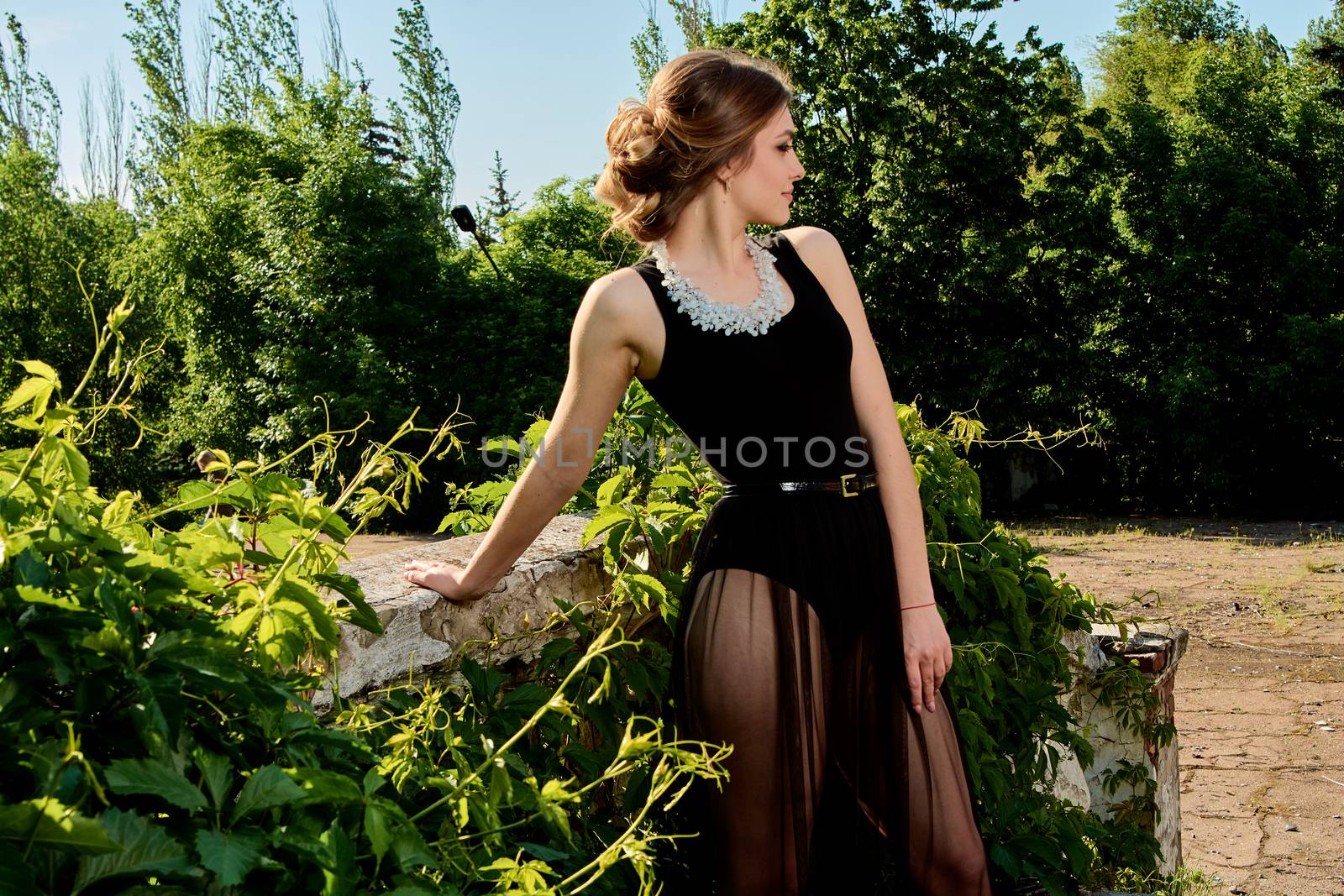 Young attractive woman in the sexy see-through, transparent, transpicuous, diaphanous, clear black dress posing at summer sunny day outdoor in the old park. Fashion woman. Young woman modern portrait.