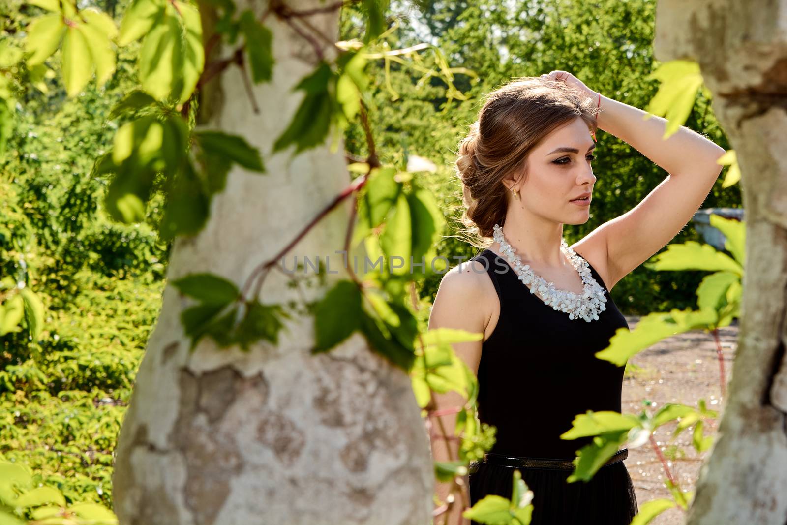 Young attractive woman in the sexy see-through, transparent, transpicuous, diaphanous, clear black dress posing at summer sunny day outdoor in the old park. Fashion woman. Young woman modern portrait.