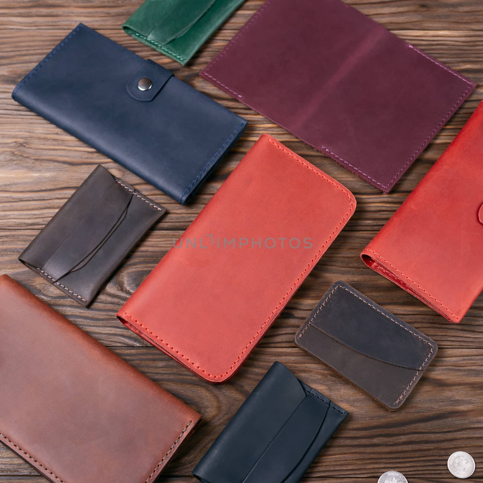 Red color handmade leather porte-monnaie surrounded by other leather accessories on wooden textured background. Side view. Stock photo of luxury accessories.