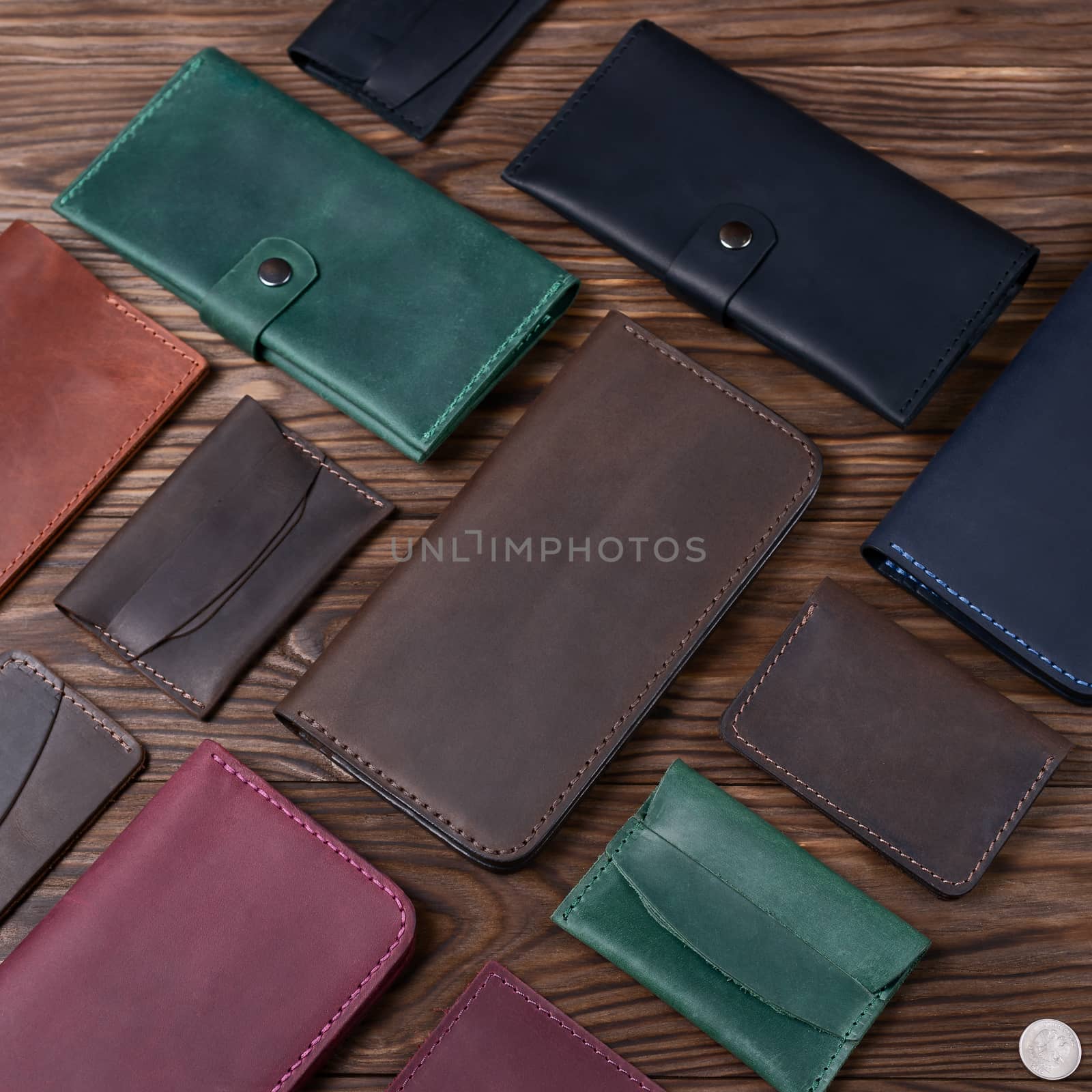 Brown color handmade leather porte-monnaie surrounded by other leather accessories on wooden textured background.  Side view. Stock photo of luxury accessories.