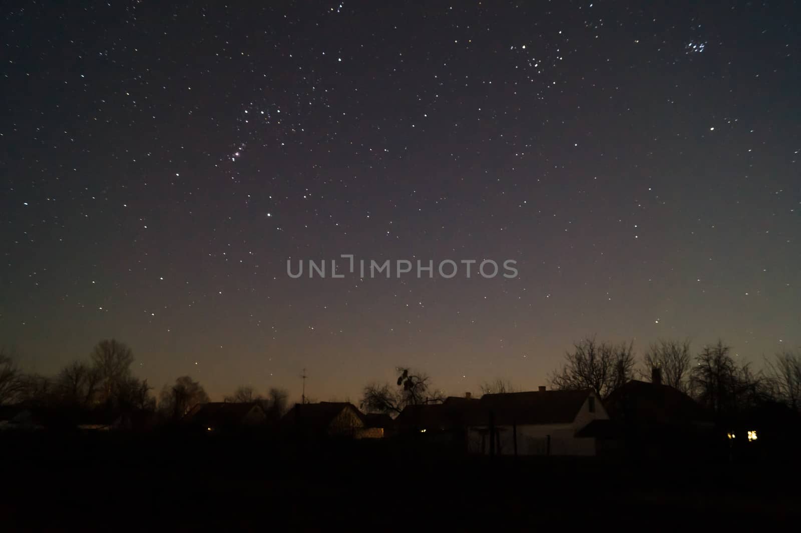 A lond exposure low light photo of village and  night sky. Village far away from city, on sky a lot of stars and constellations. Stock photo of deep sky.