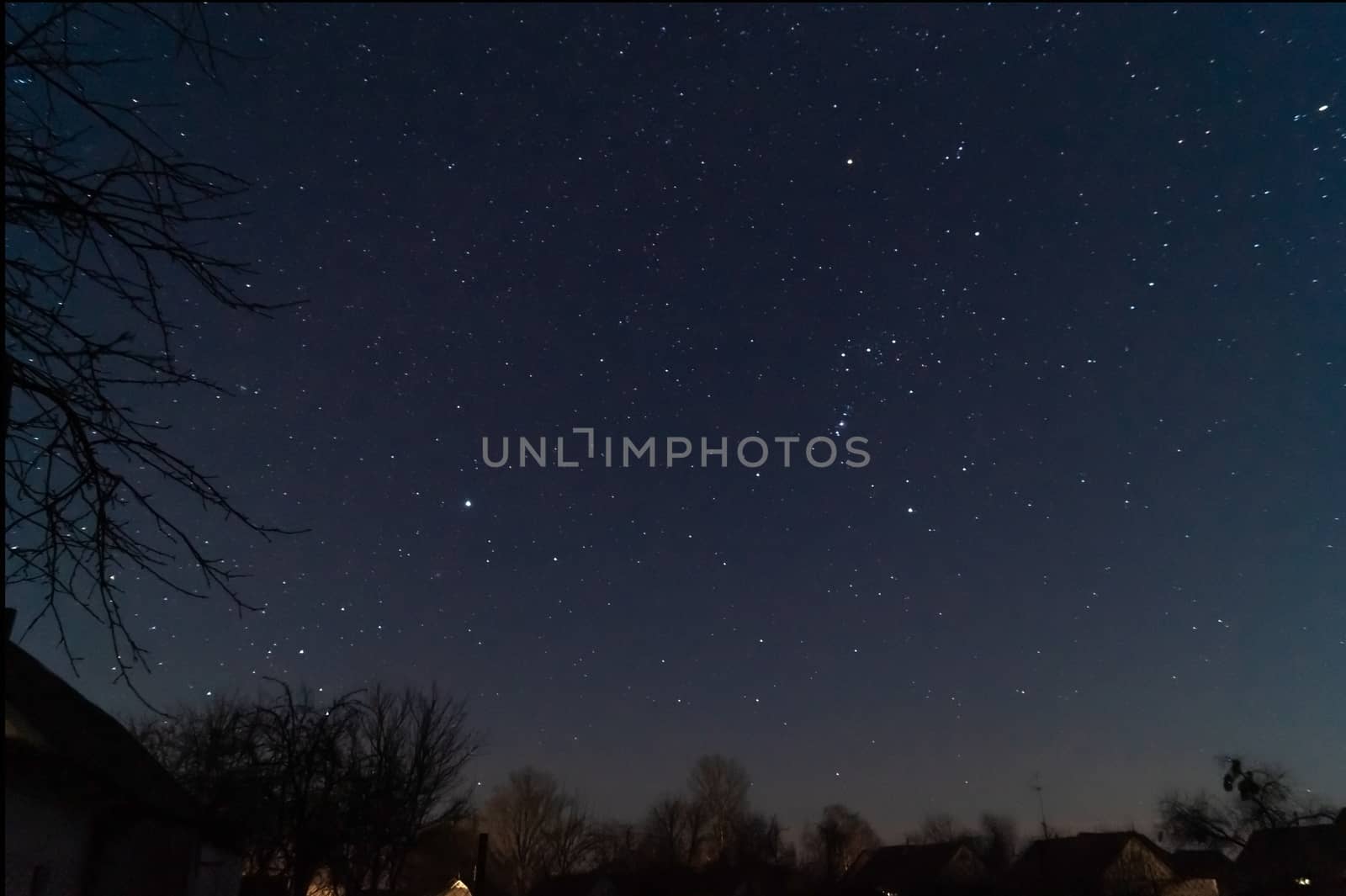 A lond exposure low light photo of village and  night sky. Village far away from city, on sky a lot of stars and constellations. Stock photo of deep sky.