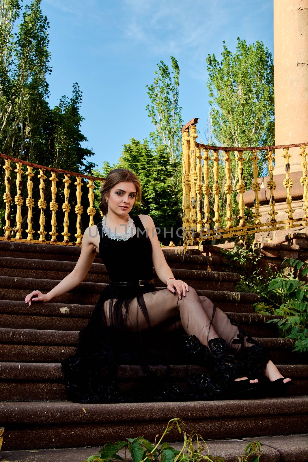 Young attractive woman in the sexy see-through, transparent, transpicuous, diaphanous black dress posing at summer sunny day outdoor at the old stairs. Fashion woman. Young woman modern portrait.