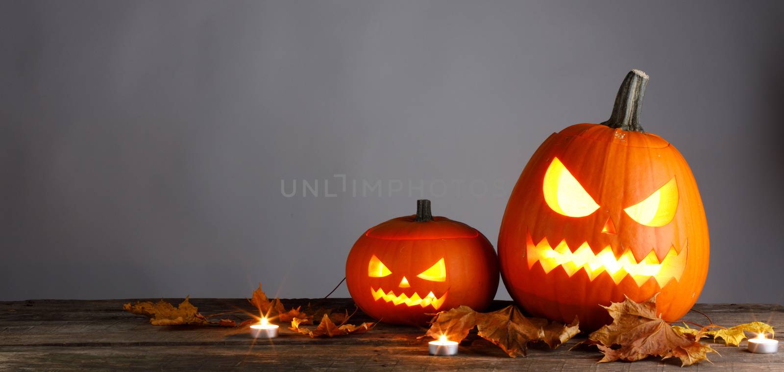 Halloween pumpkins head jack o lantern and dry maple leaves on wooden background