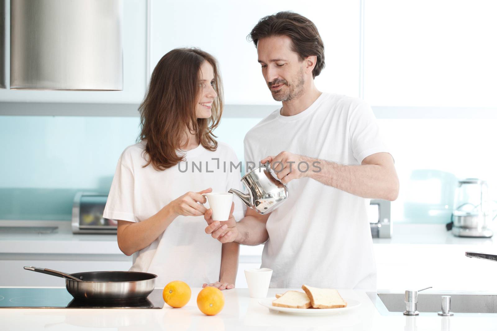 Happy couple cooking breakfast together in the kitchen and drinking coffee