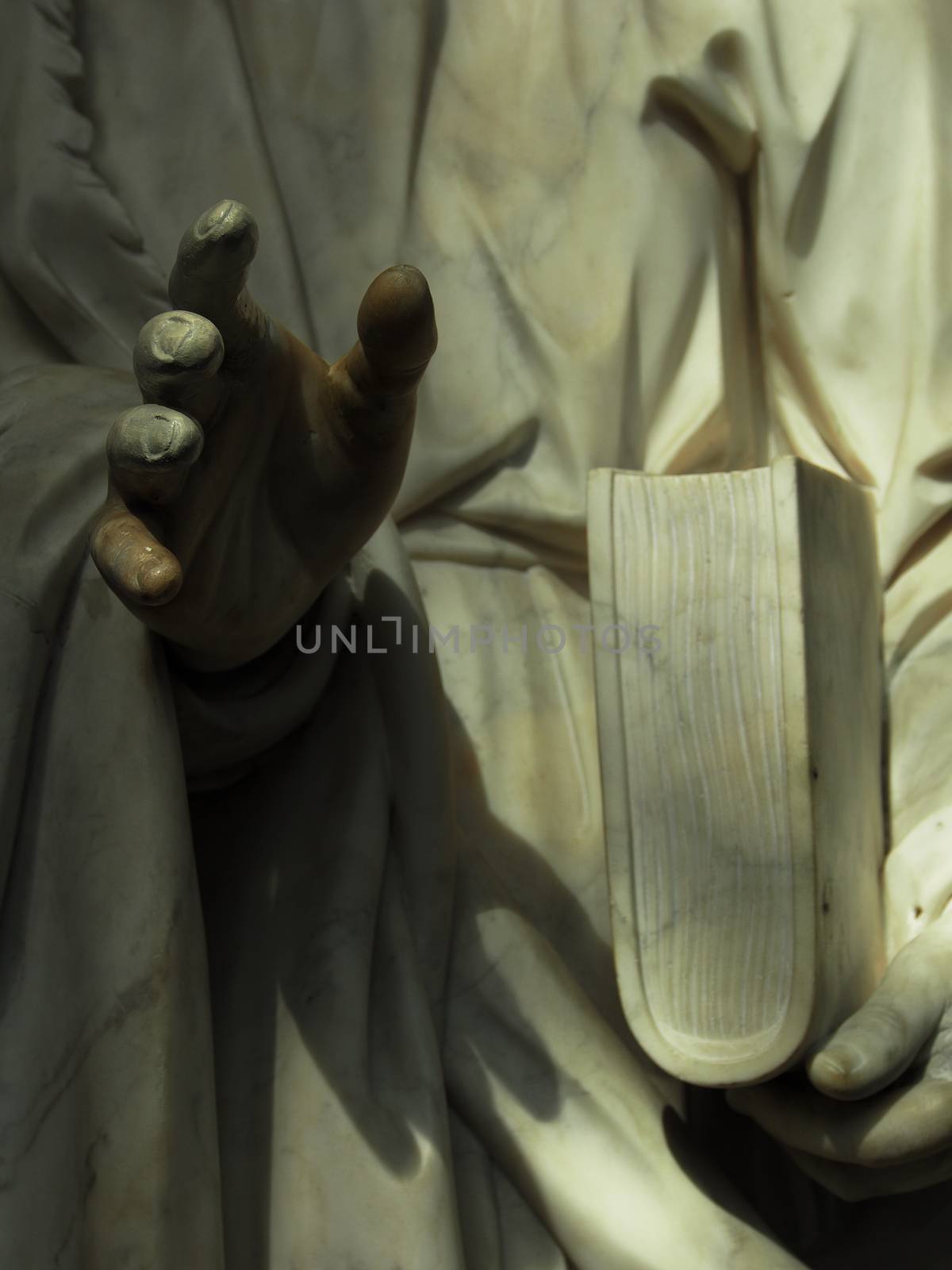 details of ancient statue, a hand and a book in low light