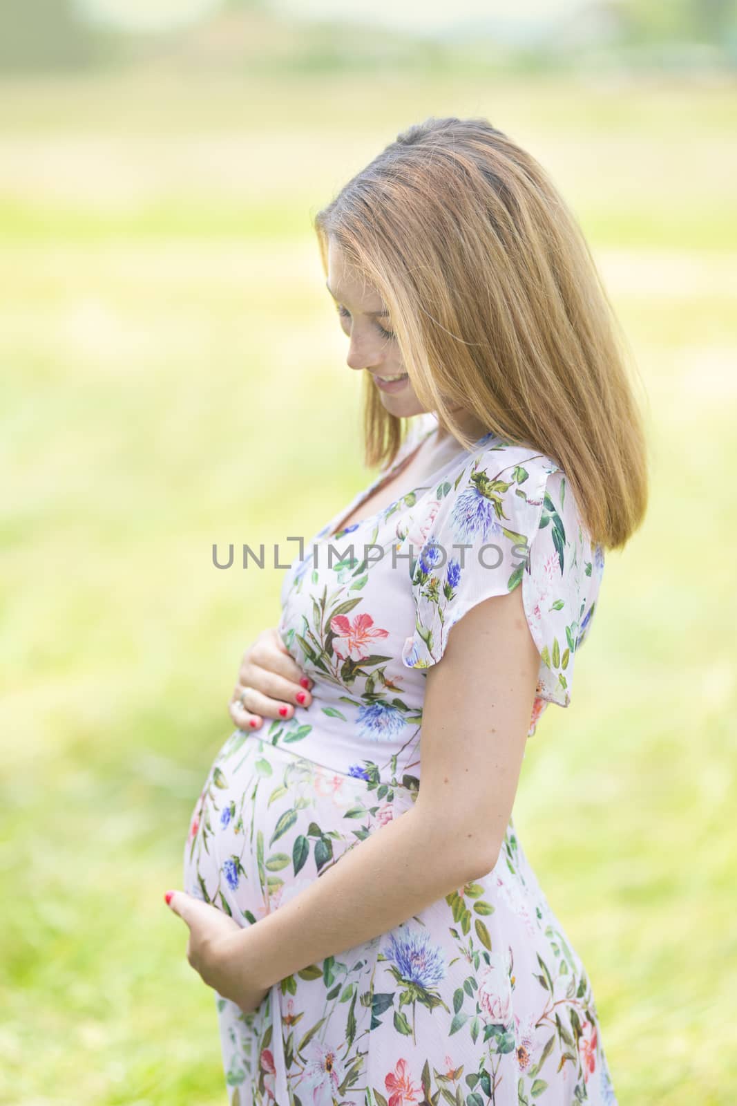 Portrait of beautiful pregnant woman in white summer dress relaxing in meadow full of yellow blooming flovers. Concept of healthy maternity care.