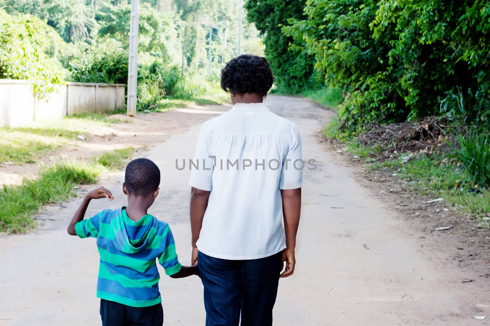 Young woman holding the hand of her  child and walk on the country road.