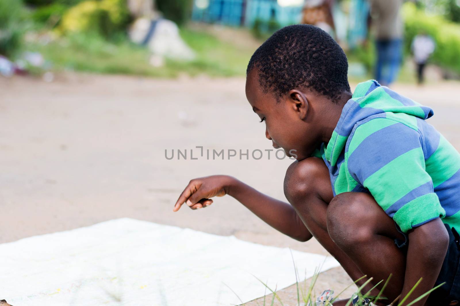 This crouching child seeks its mark on a card placed on the ground.