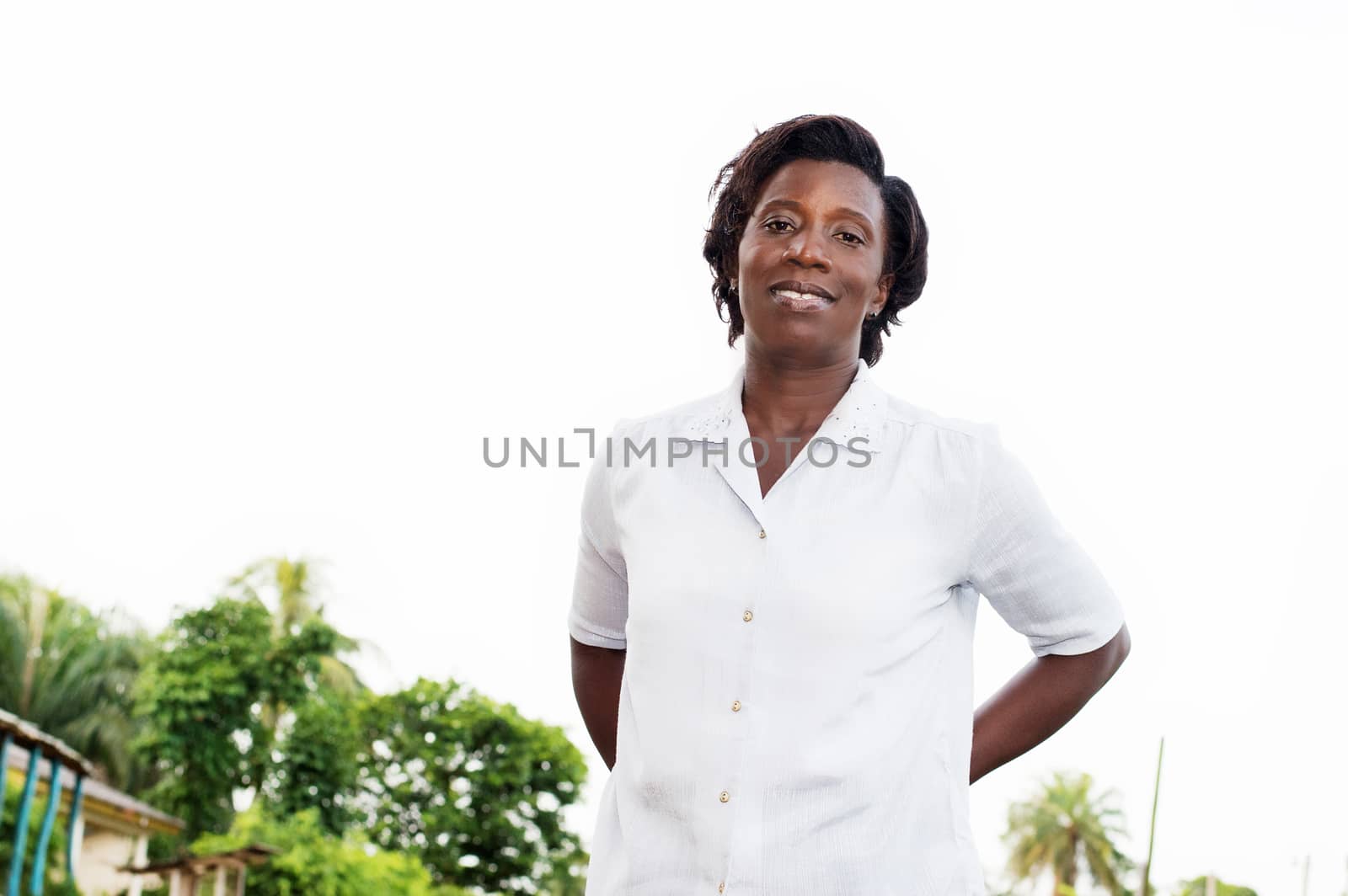smiling young woman standing outside her arms behind her back.