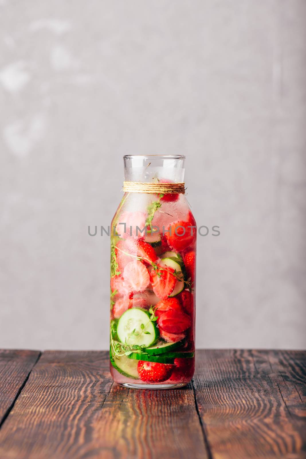Bottle of Infused Water with Fresh Strawberry, Sliced Cucumber and Springs of Thyme. Copy Space and Vertical Orientation.