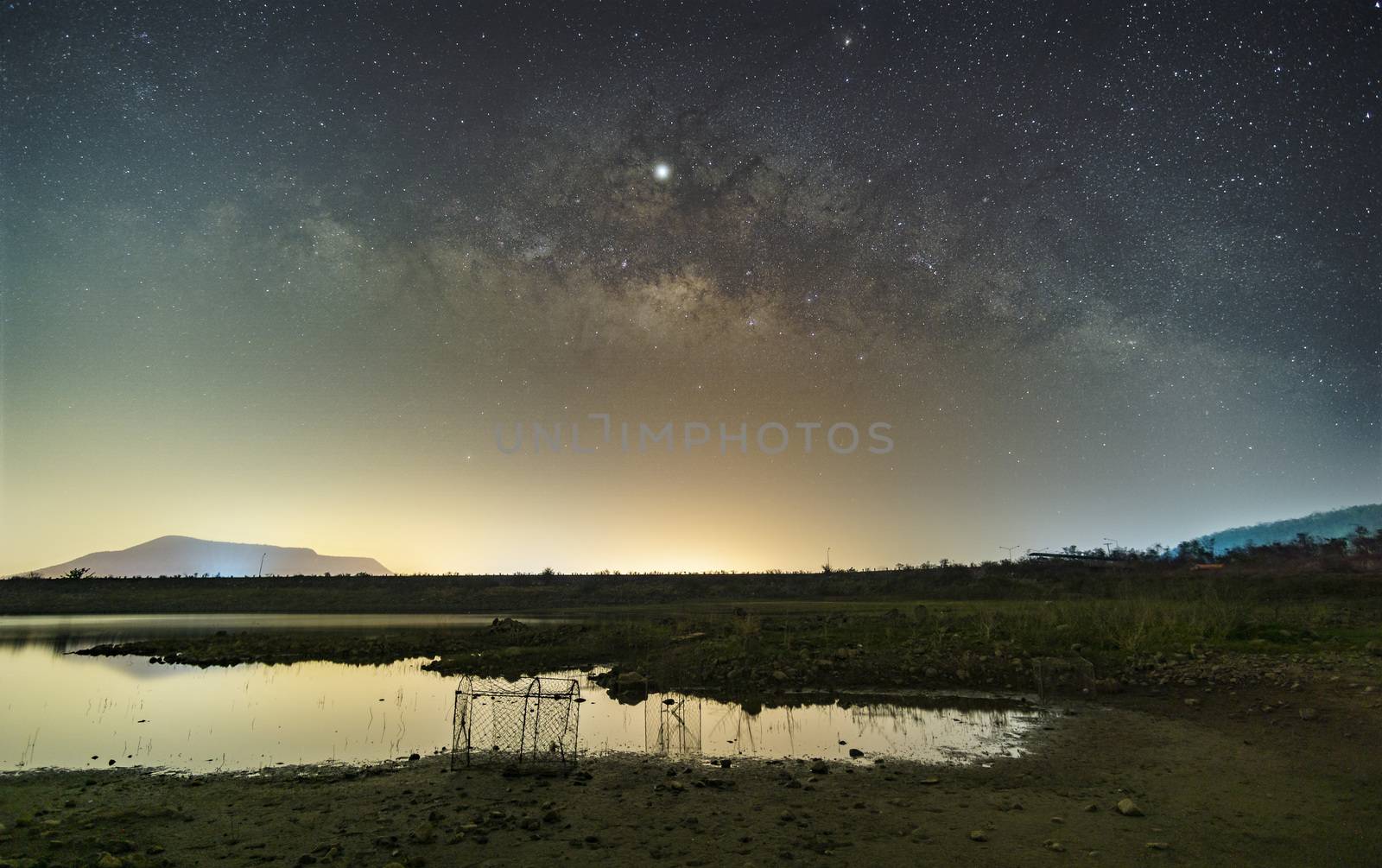 The stars in the sky reflect the light at night. The Milky Way above the mountains and the pond Mae Prachan Dam and Reservoir, Phetchaburi, Thailand