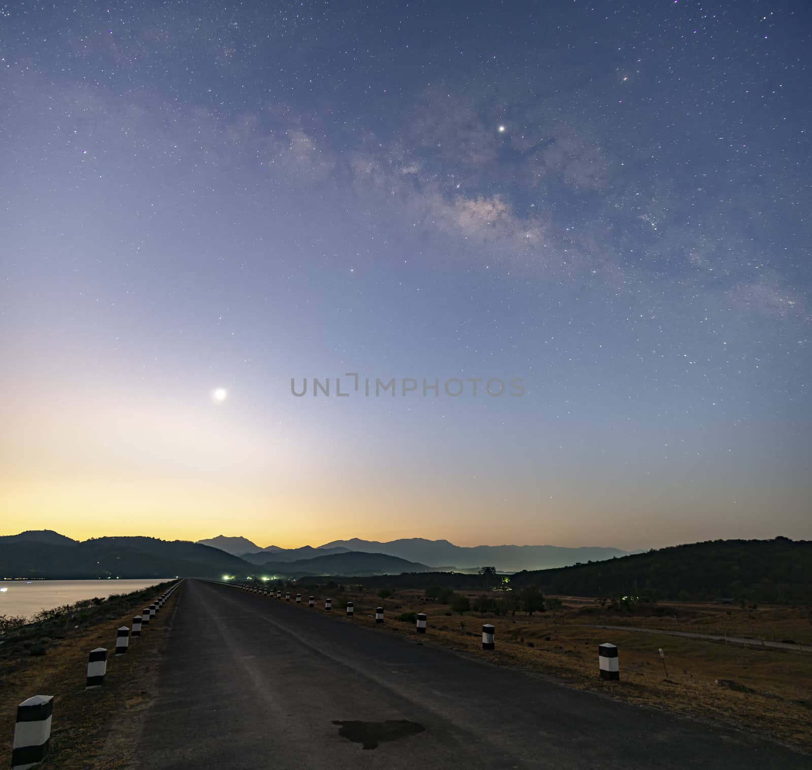 Twilight morning light Before sunrise At the reservoir, straight road ahead over the dam, the Milky Way in the early morning