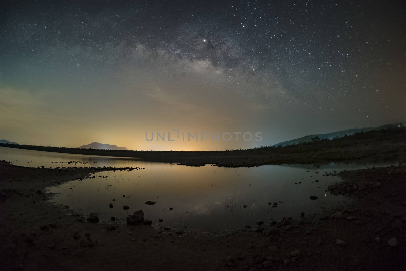 The stars in the sky reflect the light at night. The Milky Way above the mountains and the pond Mae Prachan Dam and Reservoir, Phetchaburi, Thailand