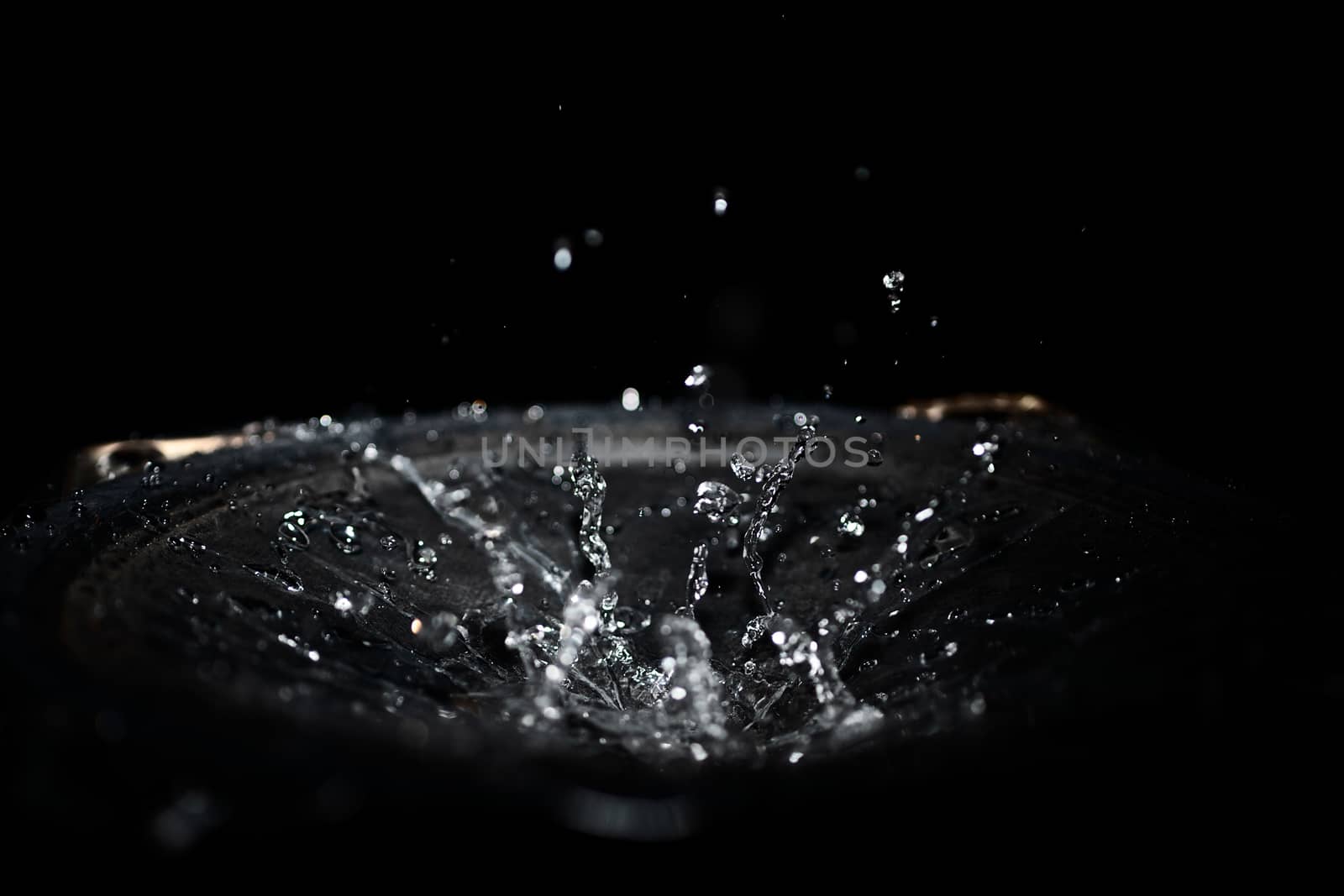 The splash of water drops in loudspeaker on black background. Perpetual motion, music and power concept.