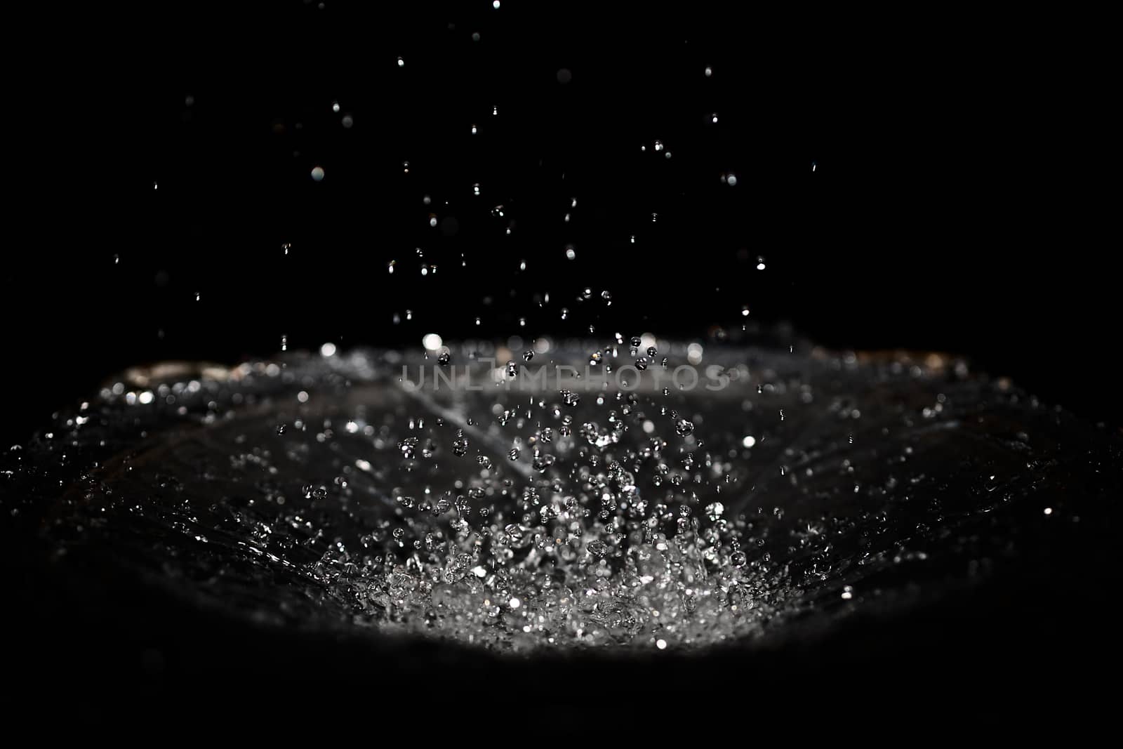 The splash of water drops in loudspeaker on black background. Perpetual motion, music and power concept.