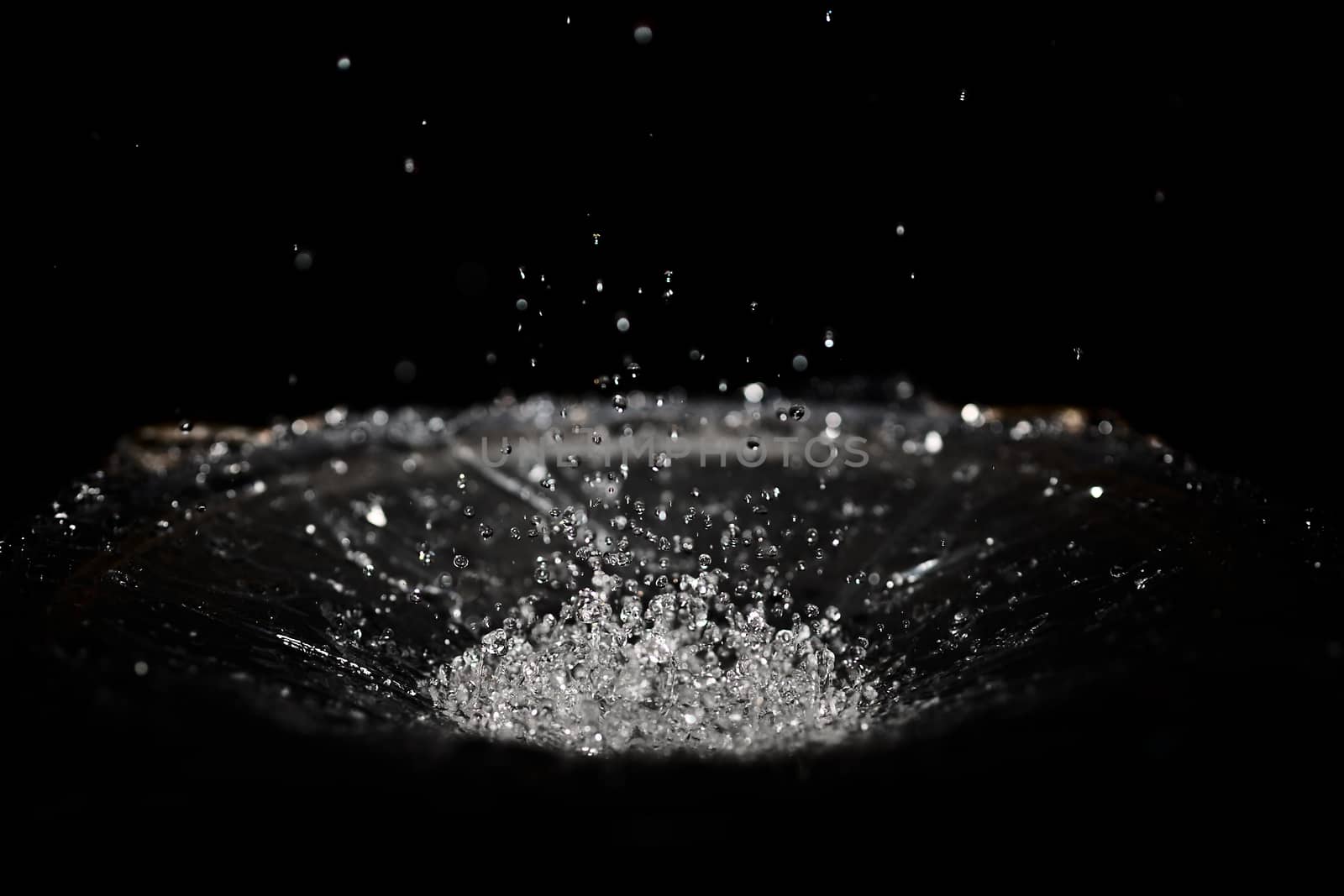 The splash of water drops in loudspeaker on black background. Perpetual motion, music and power concept.