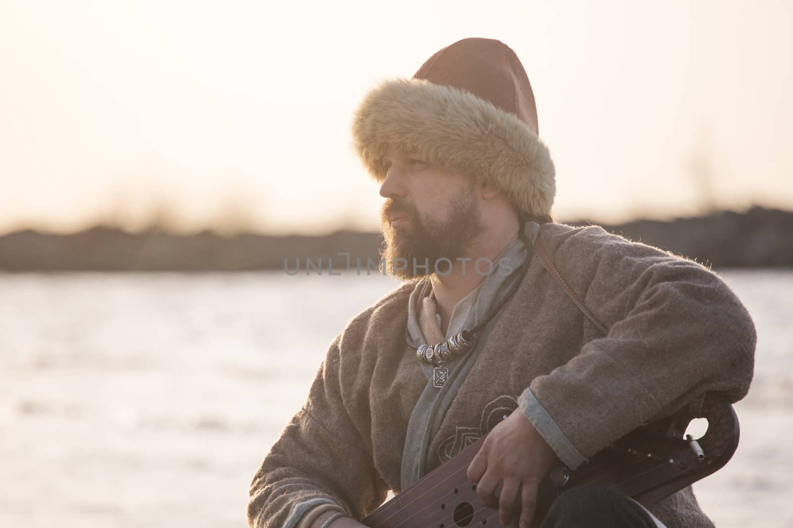 Man reencator in national costume playing gusli ancient traditional Russian musical instrument