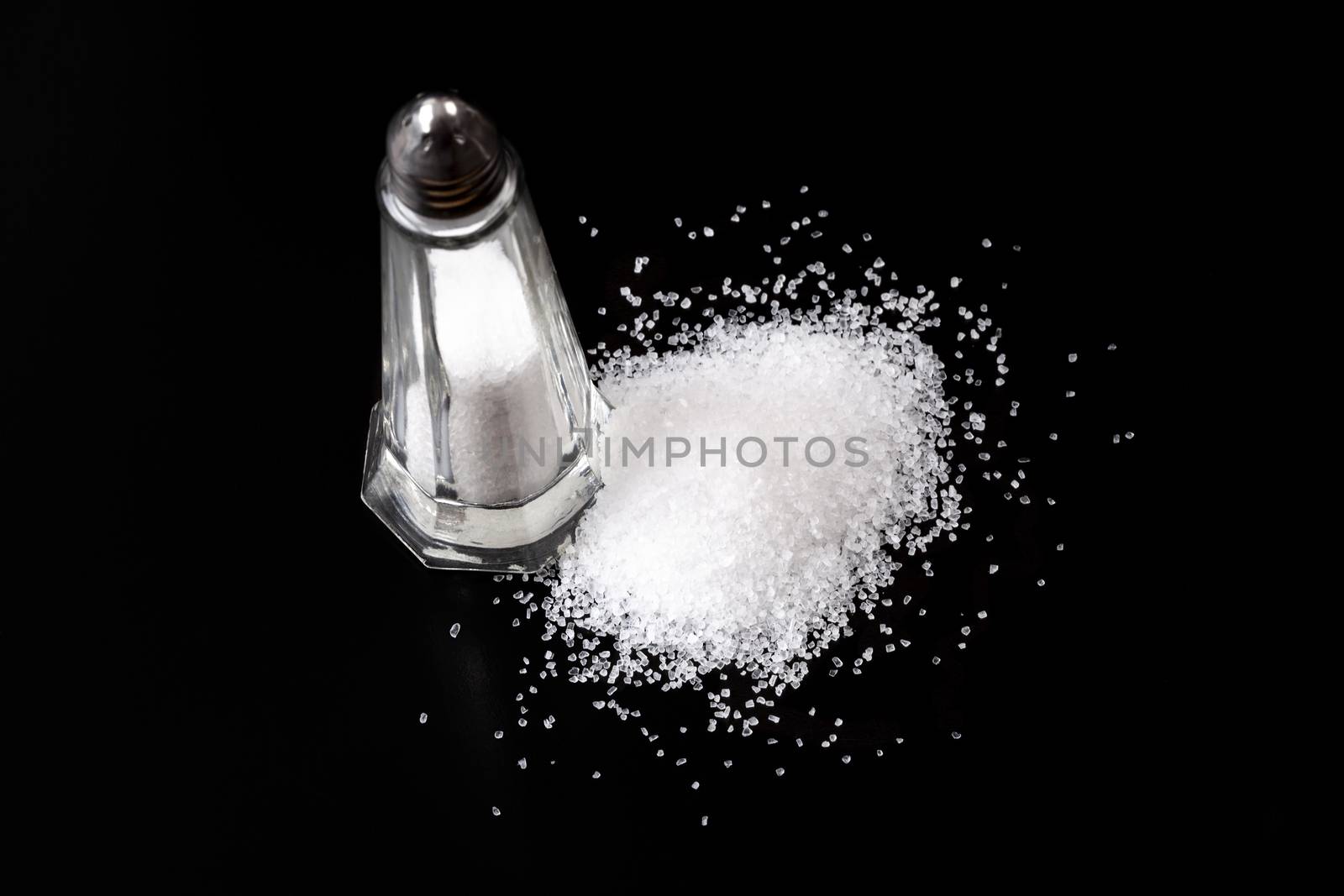 White Salt Shaker with Salt Pile On Black Background
