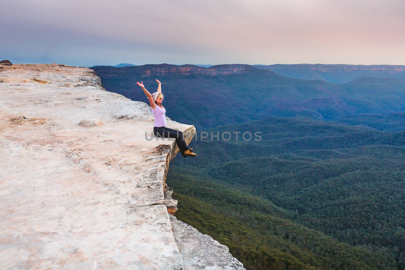 Woman showing emotional feelings of freedom and exhilaration sitting on the edge of the cliff overlooking the valley